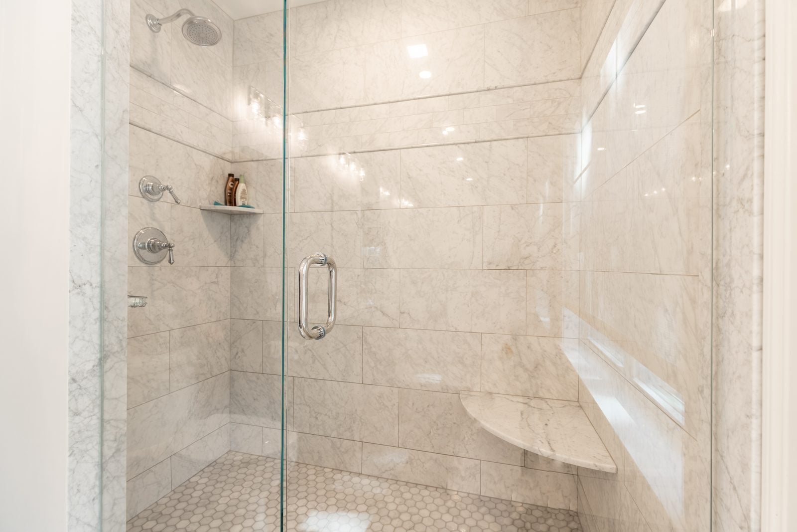Marble-tiled walk-in shower with corner seat and hex floor
