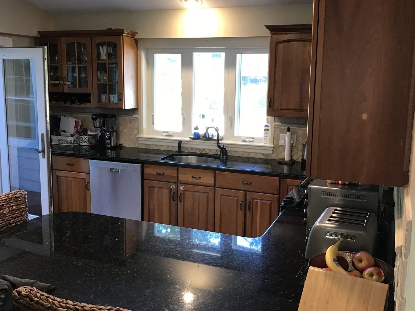 Before: Kitchen: dark wood cabinets, black granite and a peninsula gave way to painted inset cabinets, a big stone-topped island and a herringbone marble wall around the same window-lit sink wall.