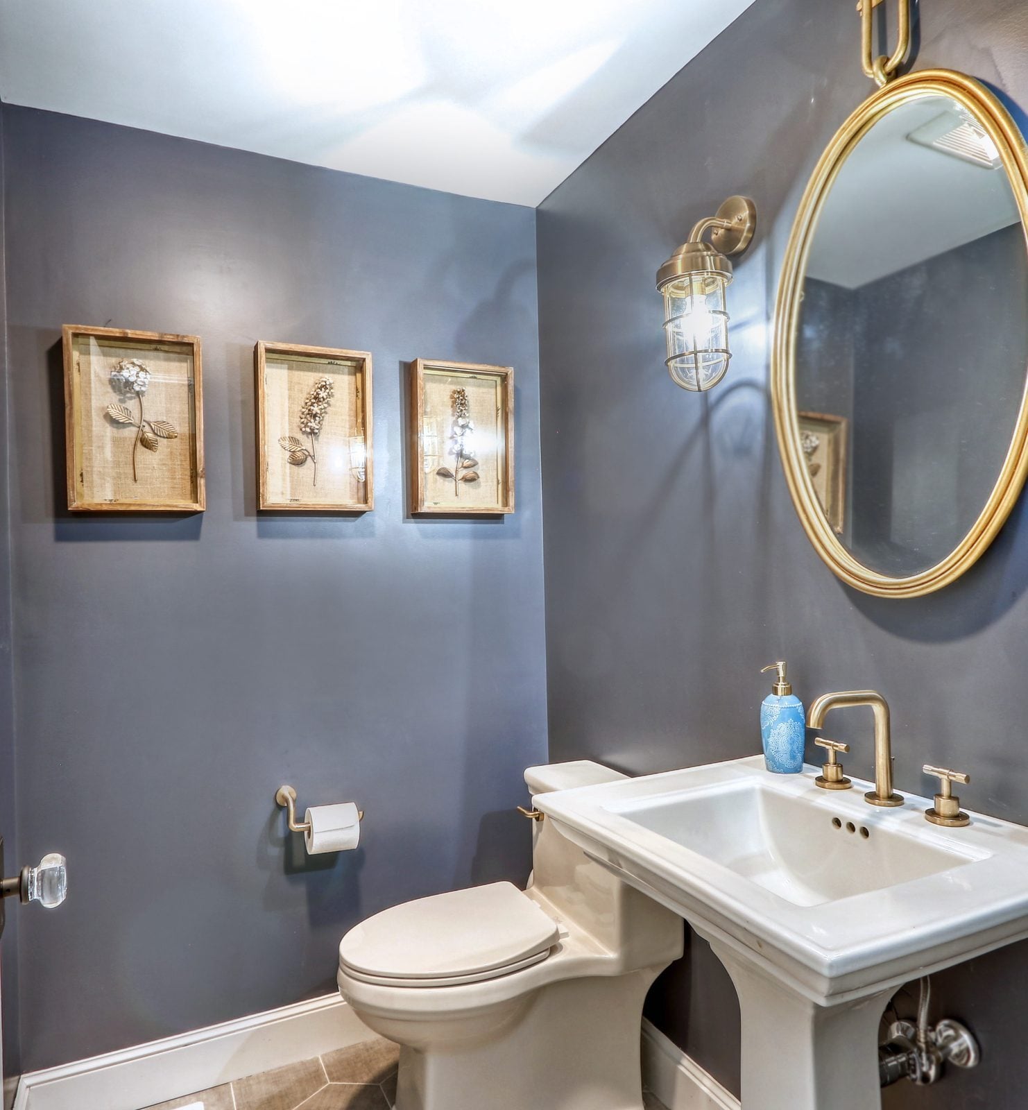 Powder room with a pedestal sink, brass fixtures and a round gold mirror