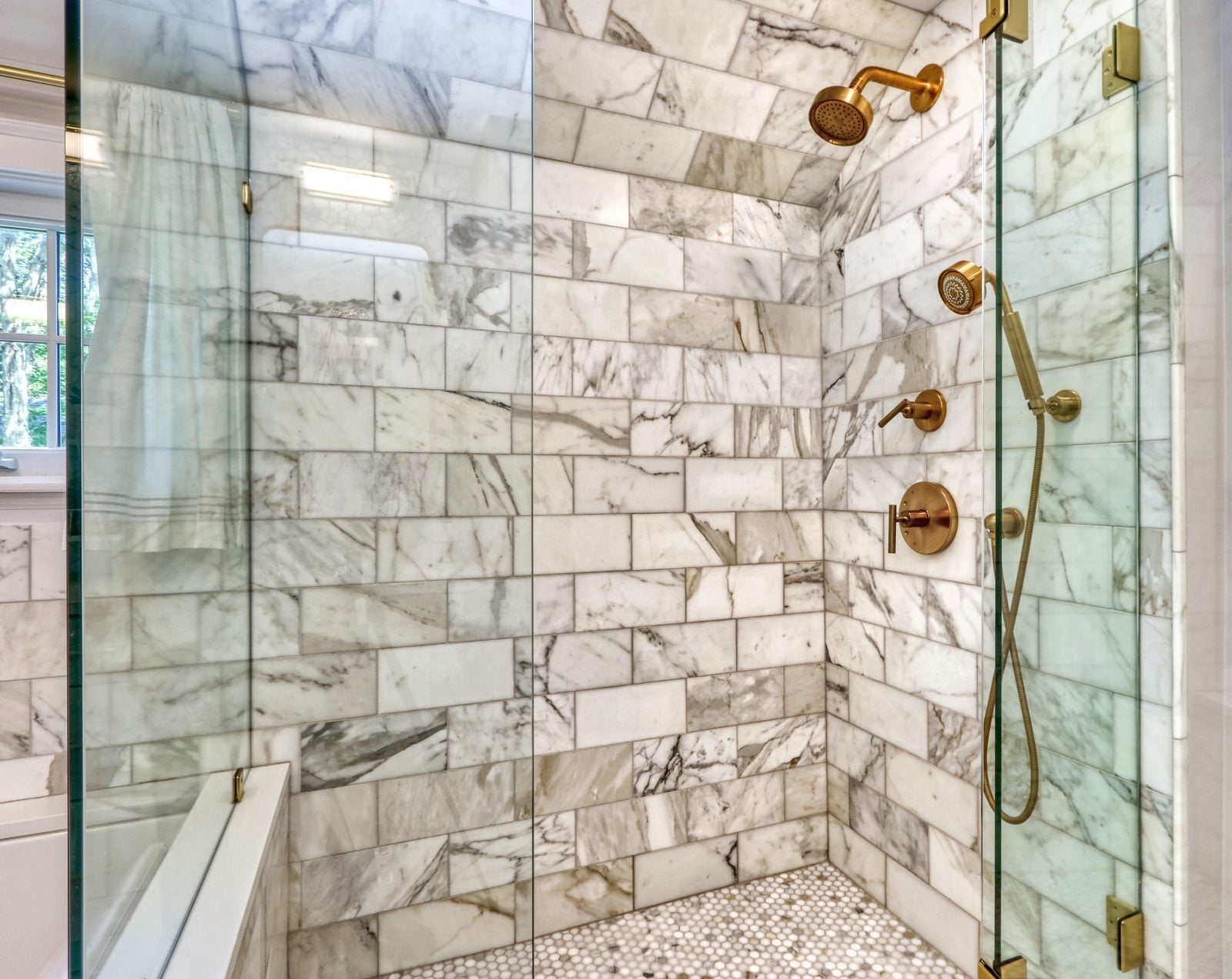 Marble-tiled shower with brass shower head, hand shower and glass enclosure