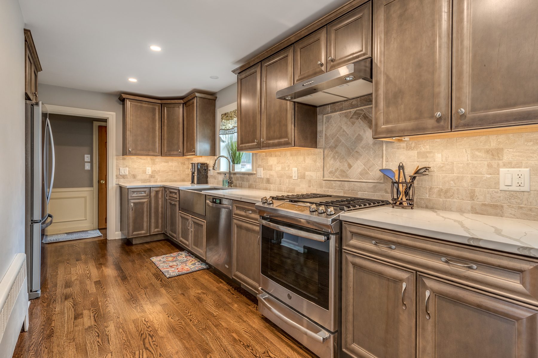 After: Kitchen: dark cabinets, laminate counters and a tile floor replaced by stained maple cabinets, quartz counters, a stainless farmhouse sink, a stone backsplash and oak floors.