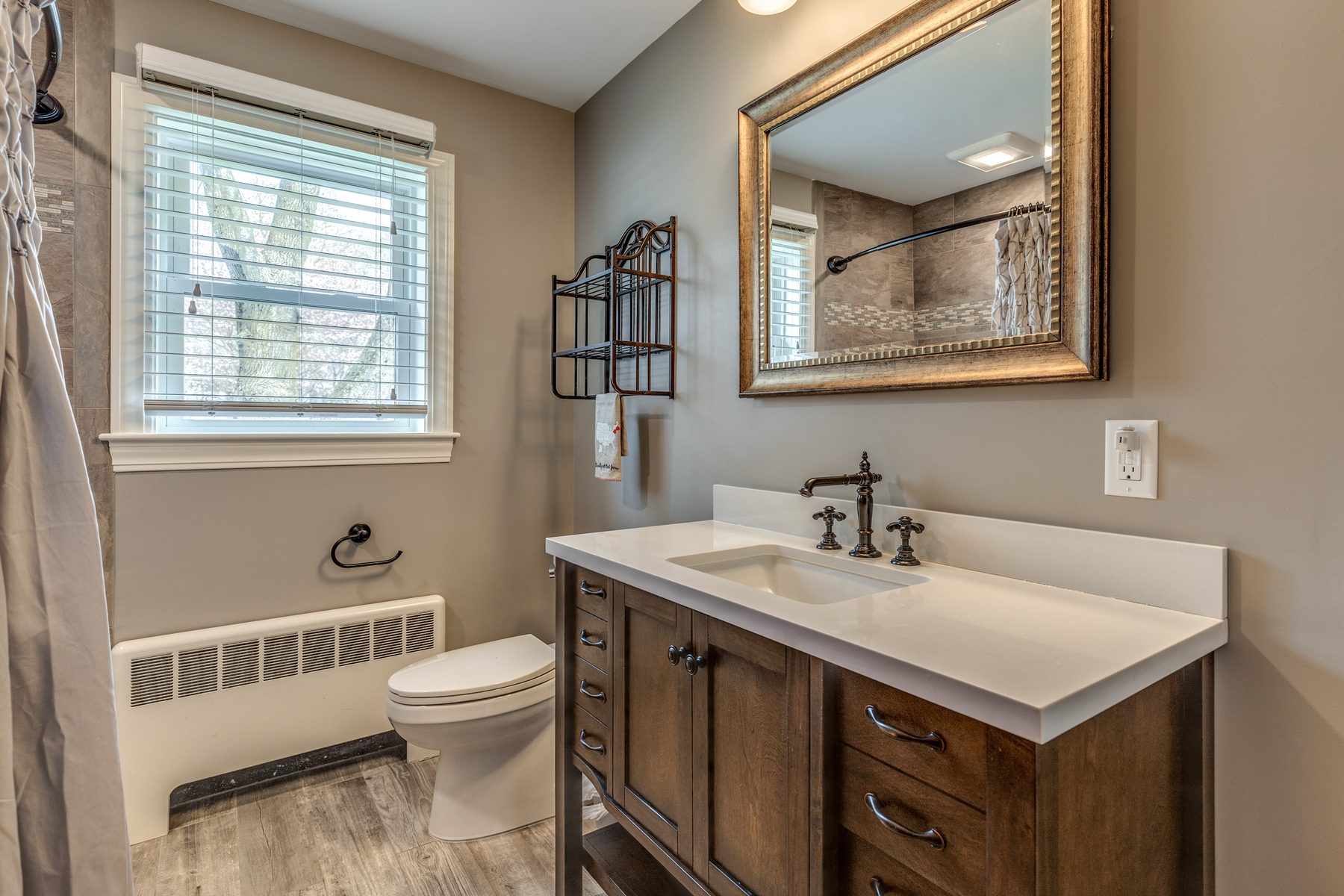 After: Bathroom: pink and black tile and an old vanity gave way to a tiled tub surround, a wood vanity with a quartz top and a wood-look tile floor.