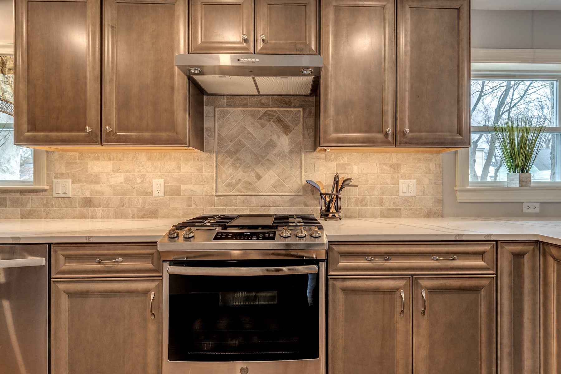 Range wall with a herringbone stone inset, under-cabinet lighting and a stainless hood in a Wakefield, MA kitchen
