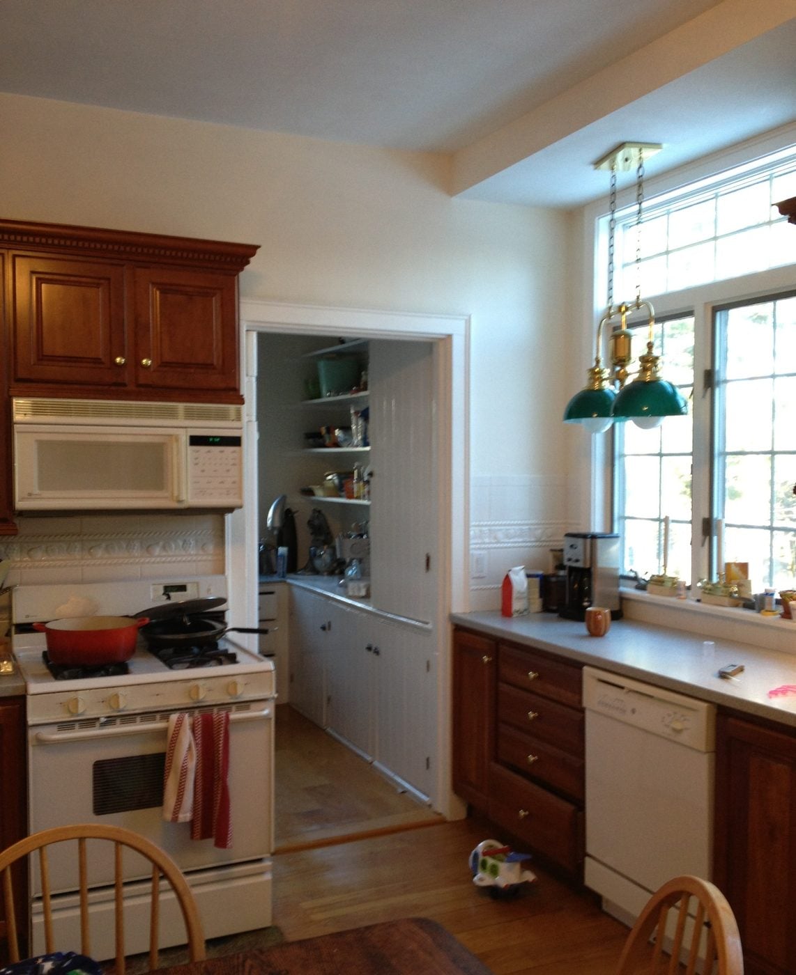 Before: Kitchen window wall: wood cabinets, a white range and a laminate counter gave way to soft gray cabinets, a stone-topped island and a glass mosaic backsplash, with the pantry doorway kept at left.