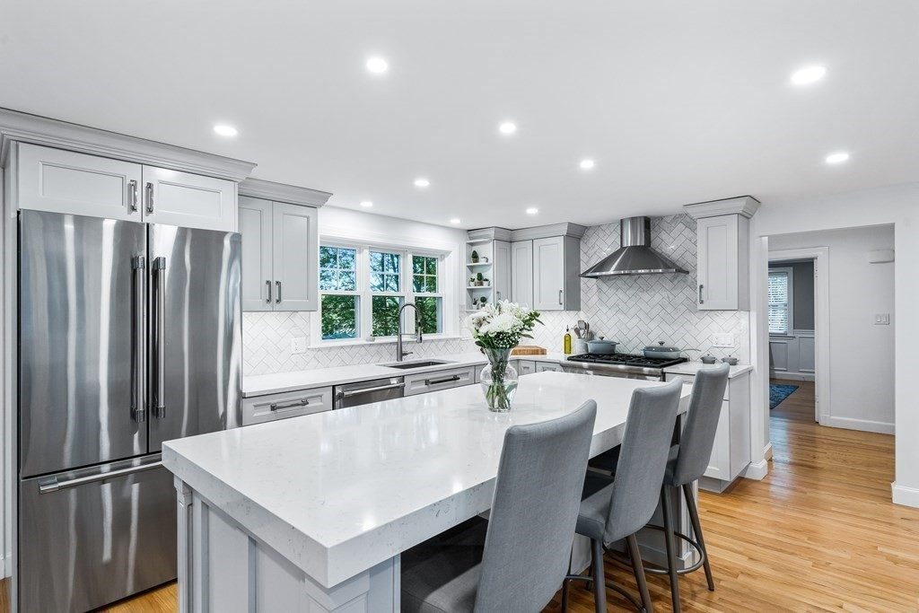 After: Sink wall: a small double window over laminate became a wider window over quartz, with a herringbone marble backsplash.