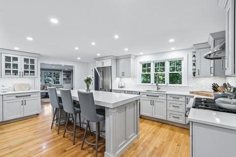 Open kitchen and island seating in Winchester, MA looking toward the family room, with gray cabinets and white quartz counters