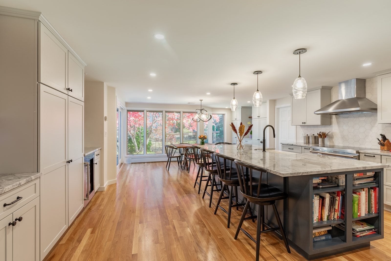Long charcoal island with open cookbook shelves and glass pendants, looking toward the dining windows in Winchester, MA