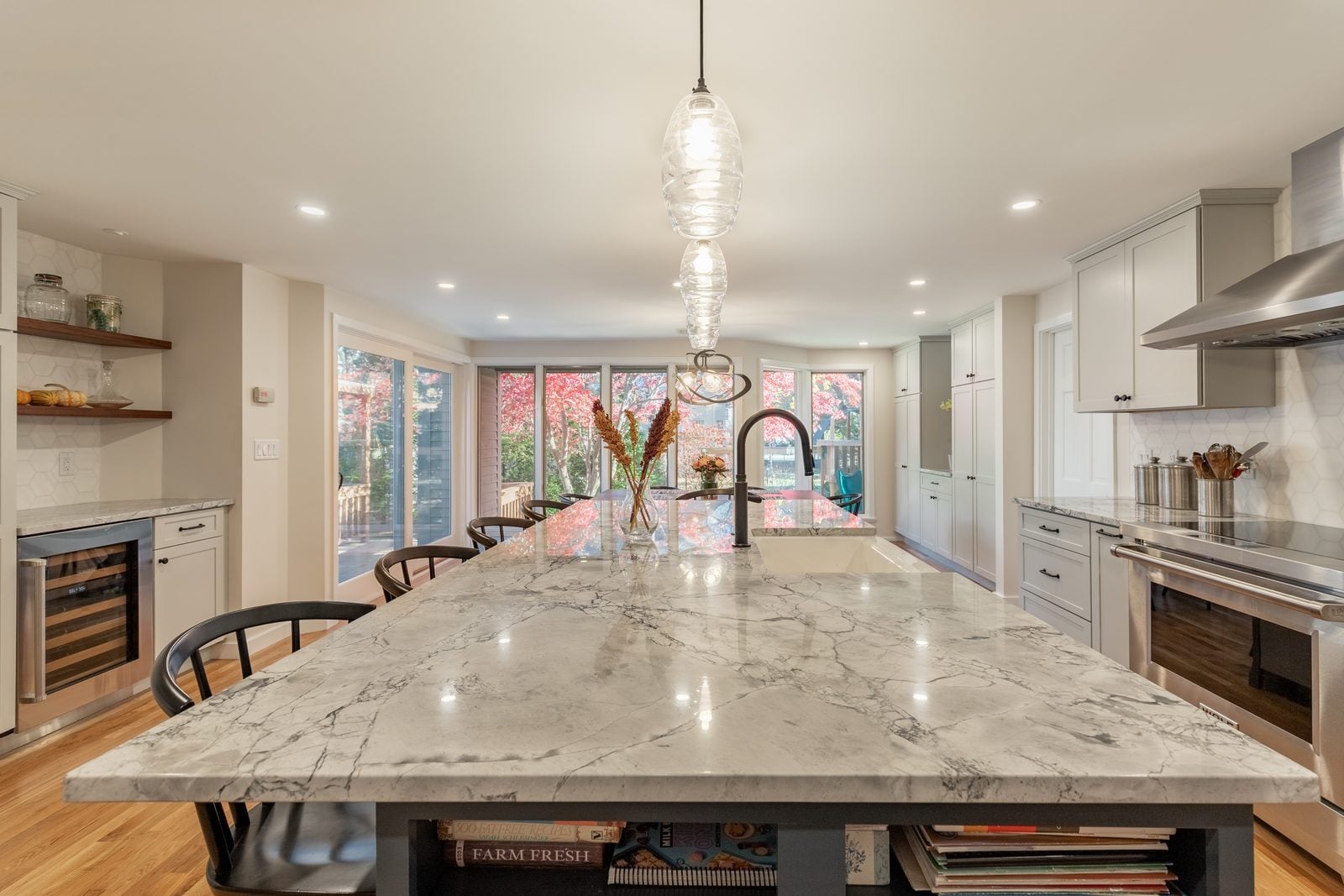 Veined white stone island top with a farmhouse sink and matte black faucet, wine cooler and range beyond in Winchester, MA